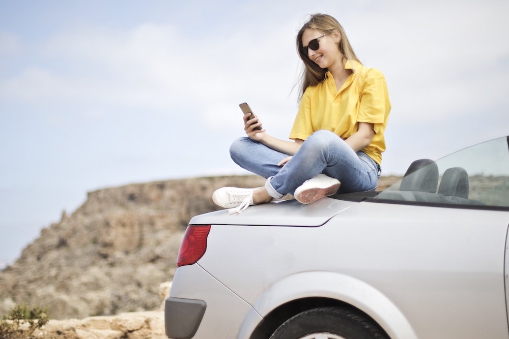 girl sitting on car looking at phone